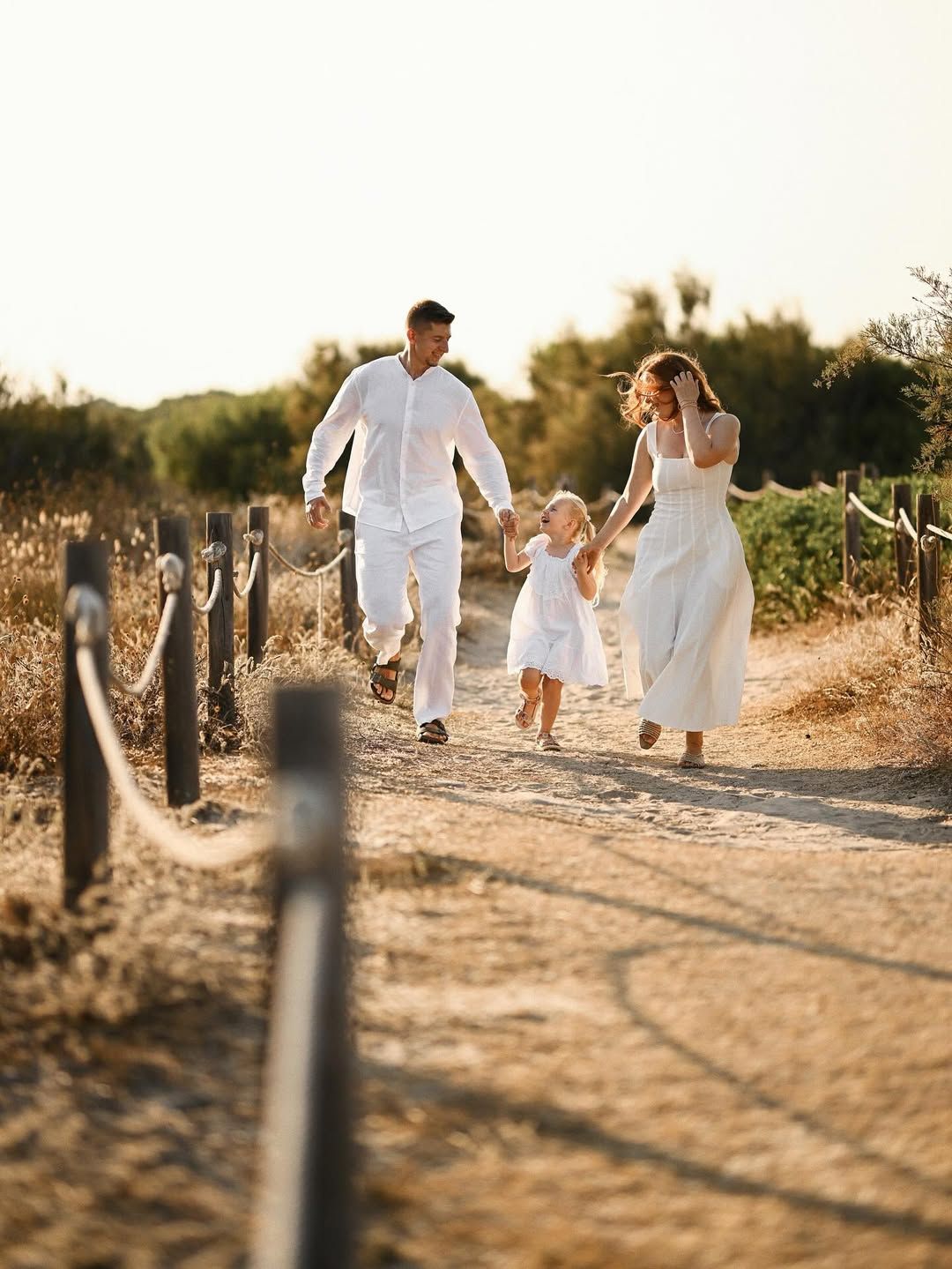A young family holding hands and running joyfully along a sandy trail in the El Saler natural reserve.