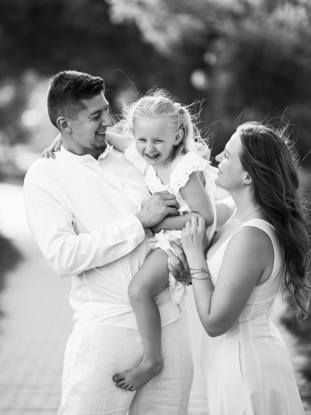 Black and white candid shot of parents laughing while holding their daughter in their arms in El Saler nature park.