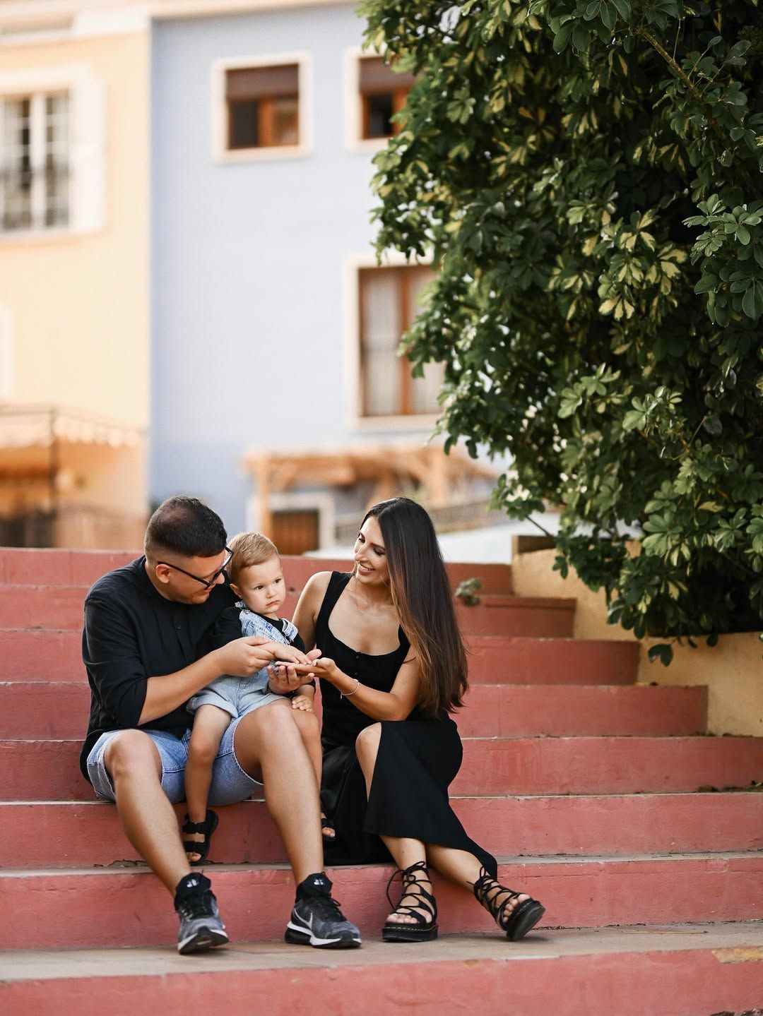 A cozy portrait of a family sitting on the stone villa steps with their little son between them in Port Saplaya, Valencia