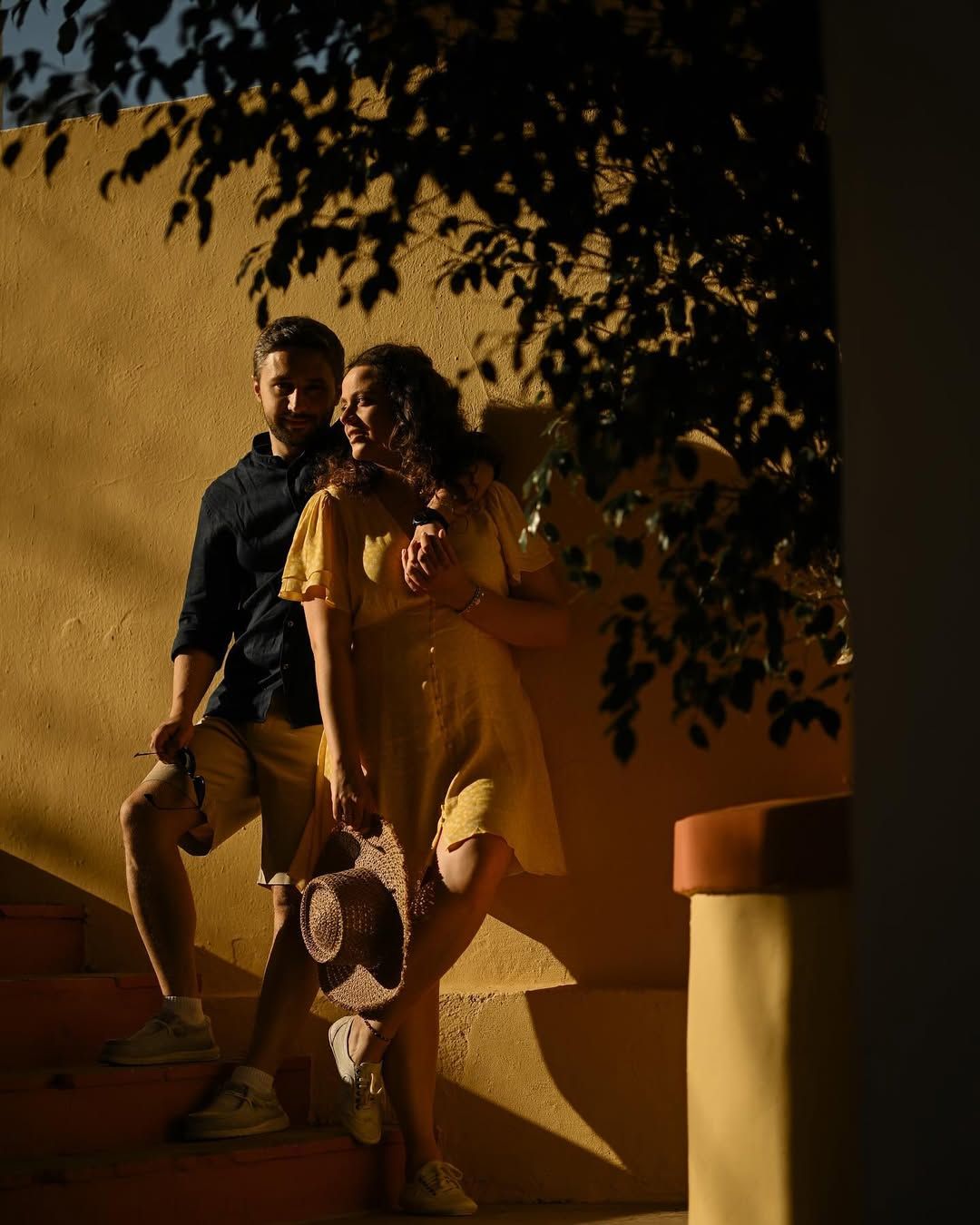 A couple posing together during golden hour sunset light against the bright yellow walls of the Port Saplaya coastal village
