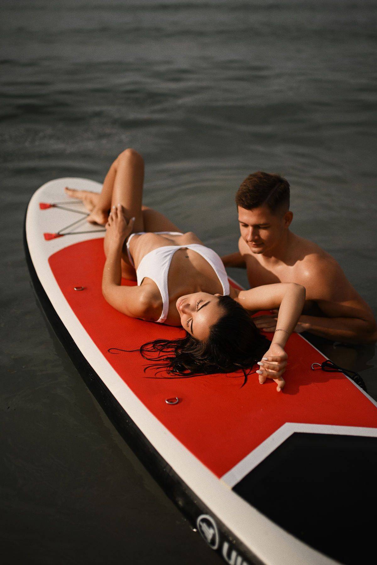A woman relaxing gracefully on a paddleboard in the clear waters of Moraira while her partner swims beside her