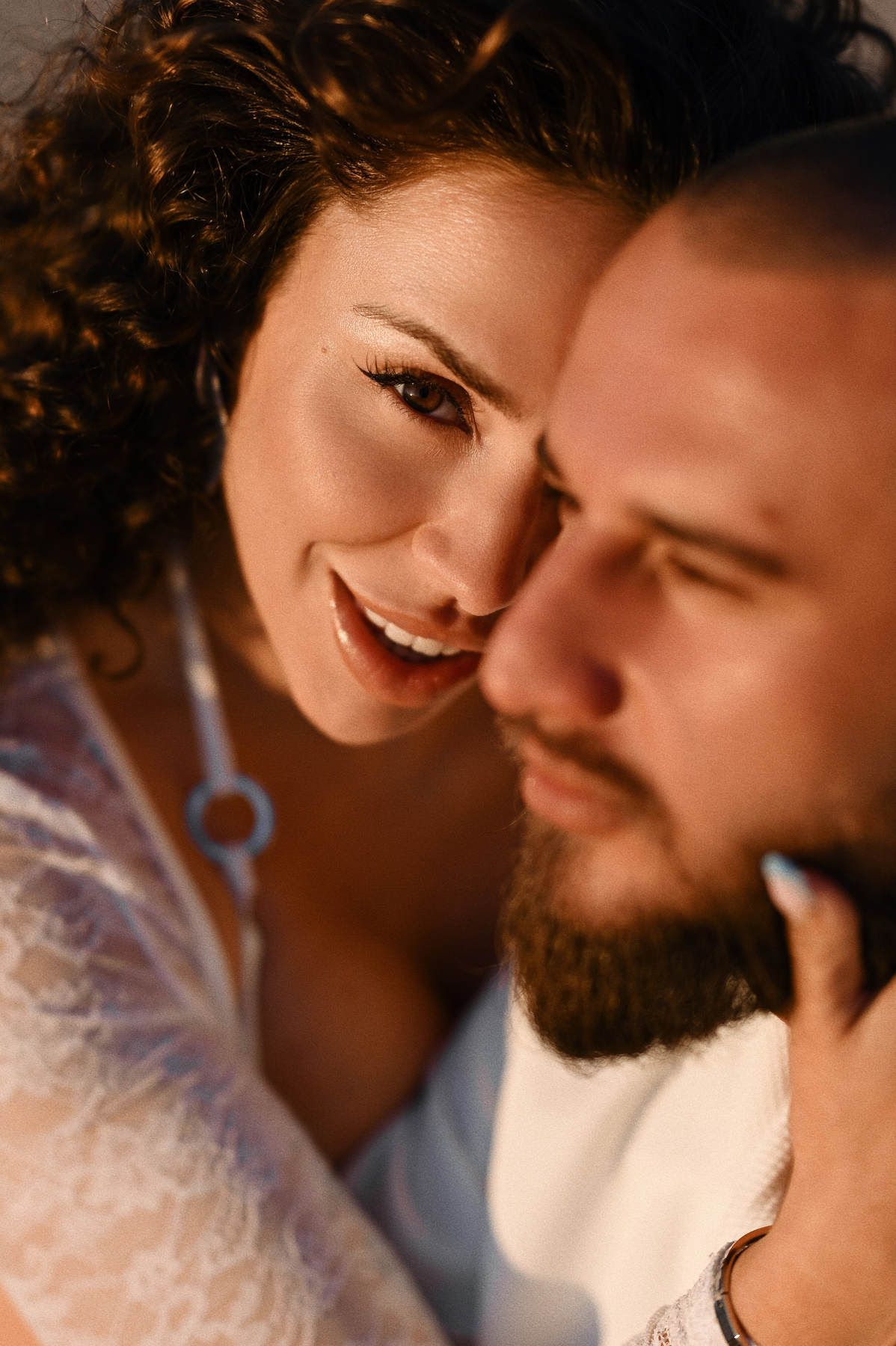 A soft, romantic close-up portrait of a pregnant woman looking at her partner with love during their beach photoshoot.