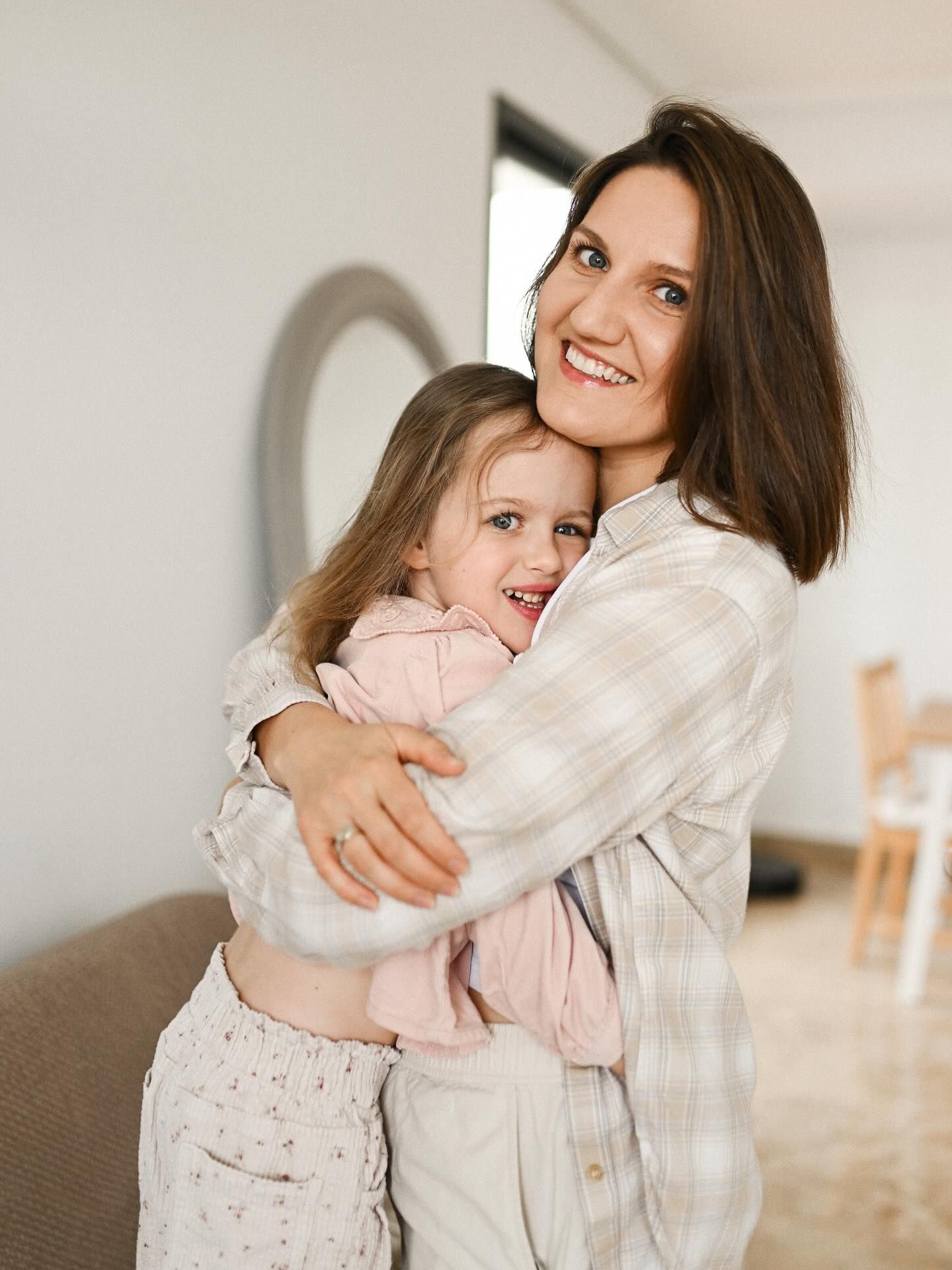 A beautiful and intimate portrait of a smiling mother warmly hugging her young daughter at home, showing their deep family connection.