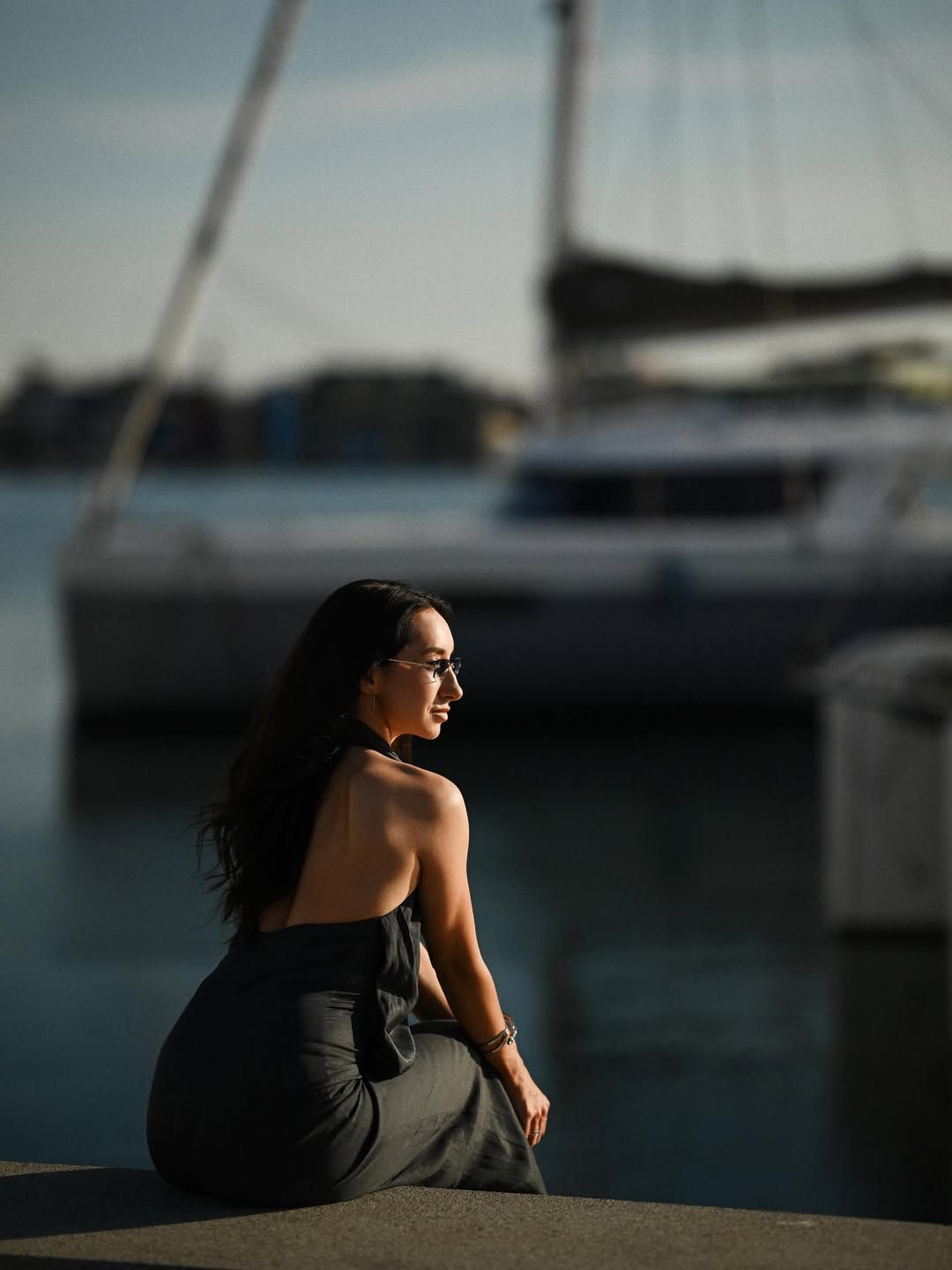 Elegant woman in a dark dress sitting by the canal with yachts in the background at Valencia Marina