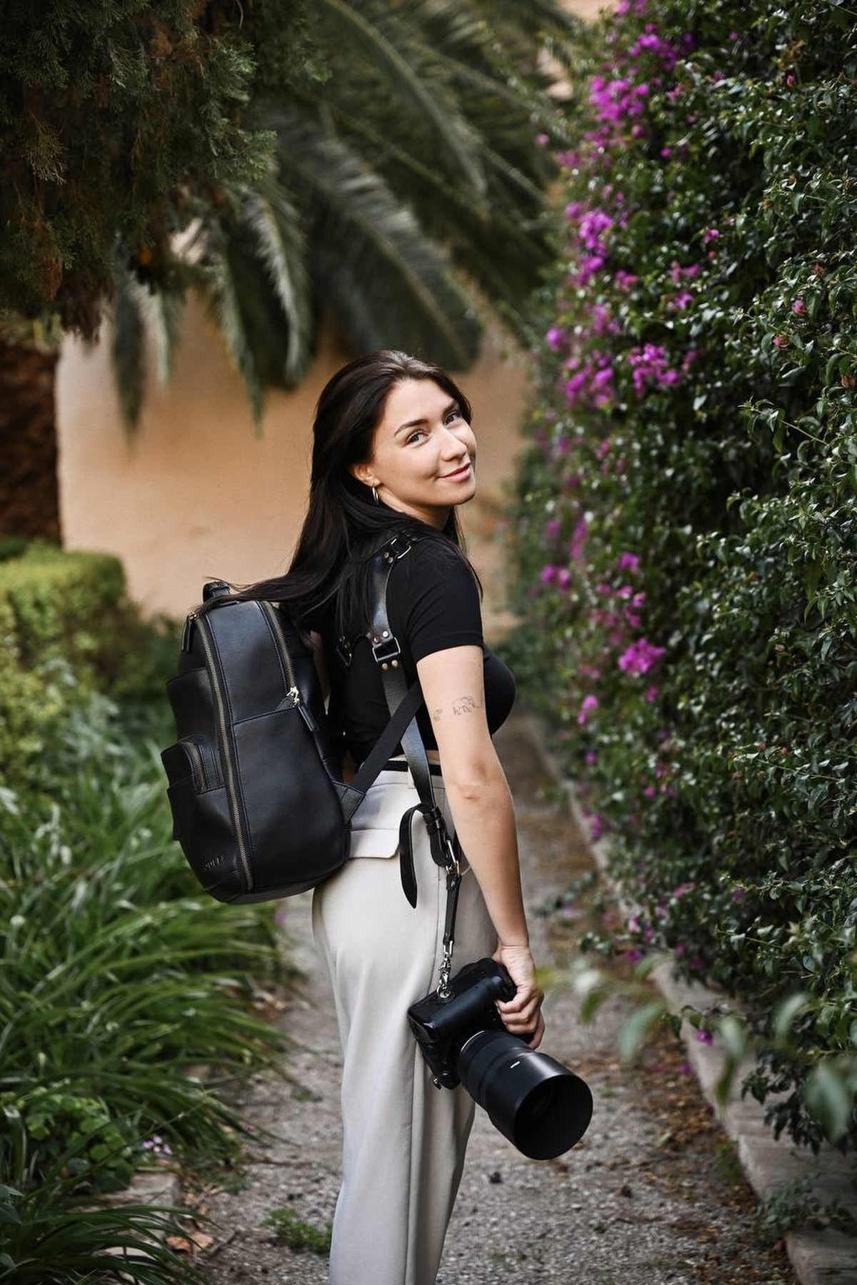 Profile portrait of Valencia photographer Darina Derzkaya with her professional camera gear and leather harness in a garden path.