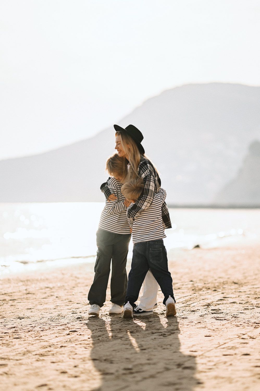 A mother and her two boys sharing a warm group hug on the sandy beach bathed in golden sunlight during a Calpe photo session.