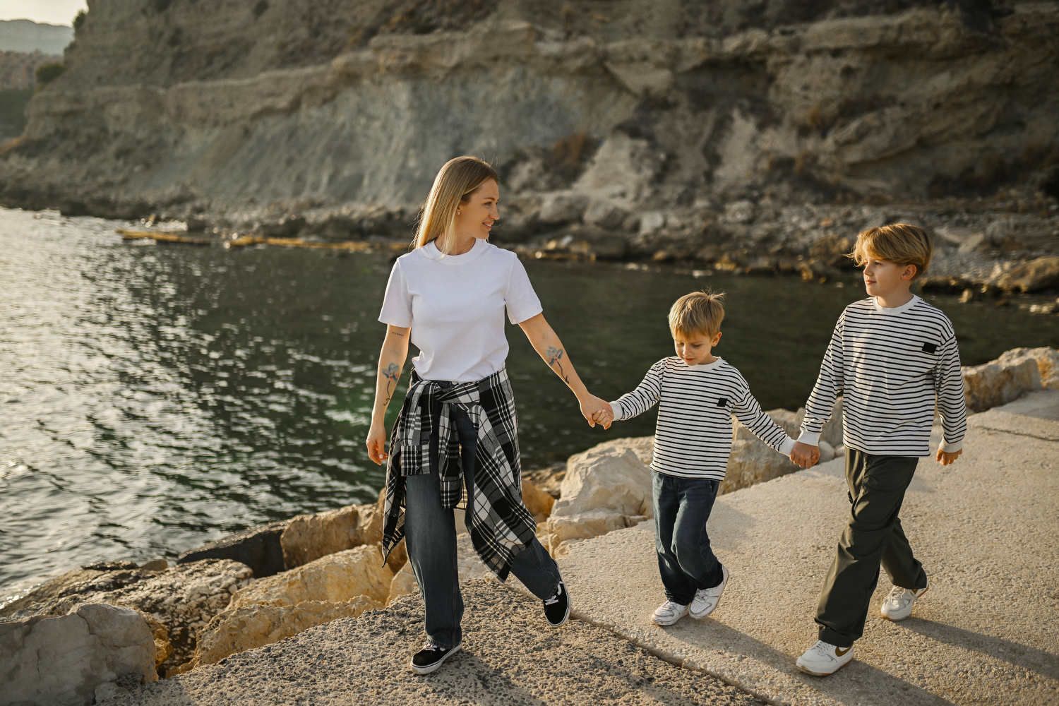 A mother and her two sons holding hands and walking along a stone pier by the sea during a lifestyle family session in Calpe