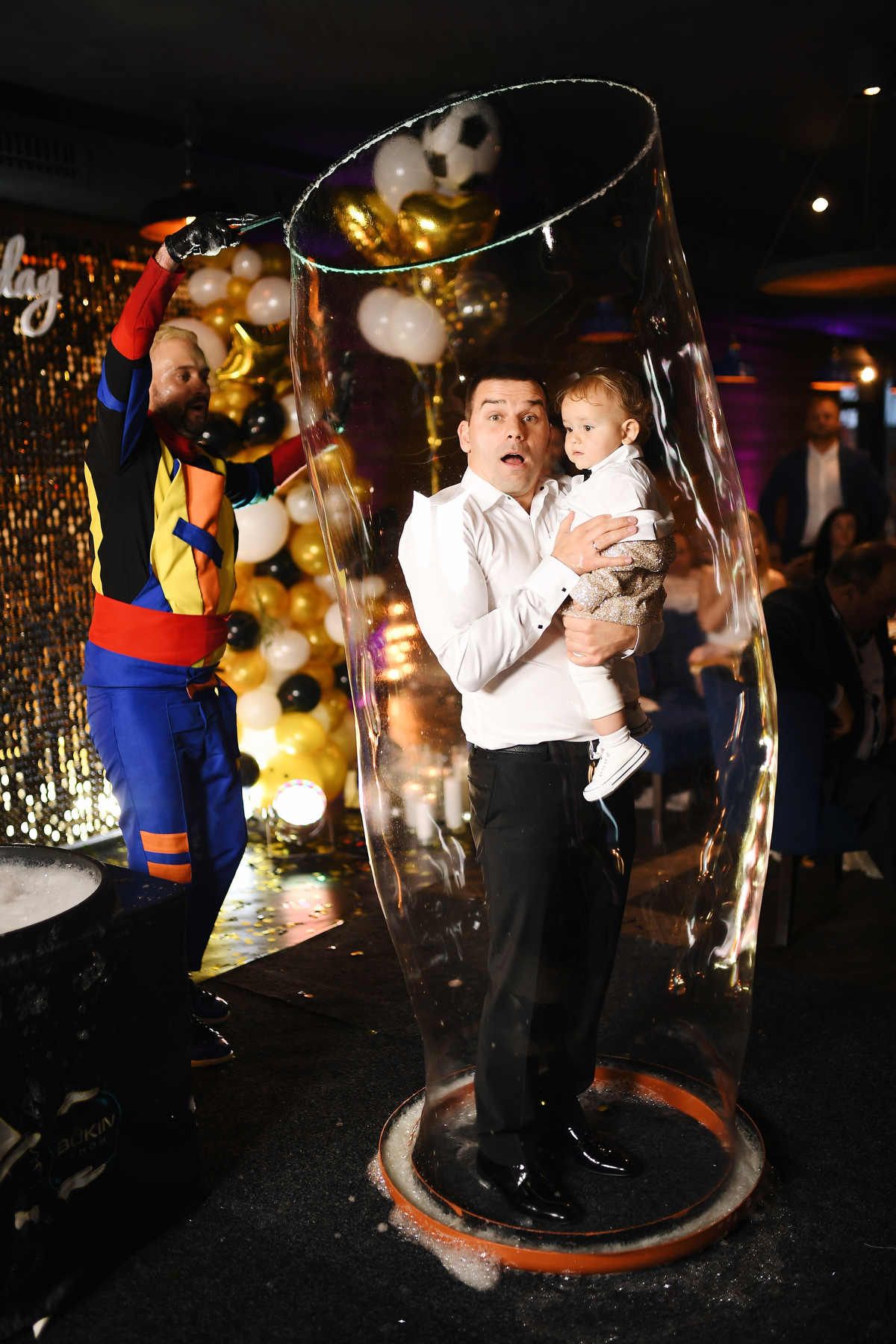 An animator performing a giant soap bubble show with a father and his baby boy standing completely inside a huge bubble.