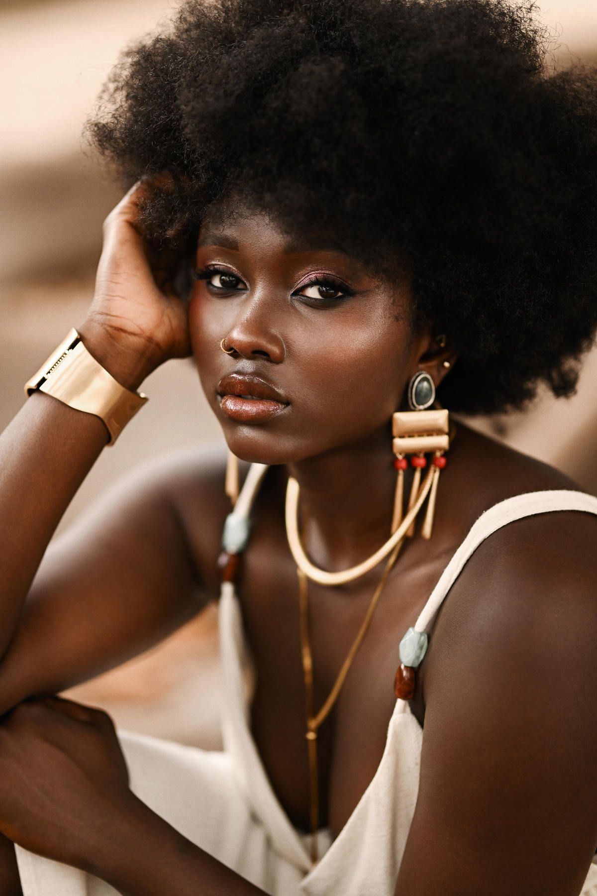 Exquisite solo portrait capturing a model looking directly at the camera, wearing bold gold accessories under a soft canopy.
