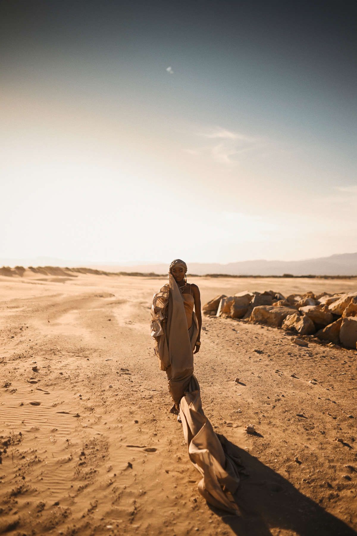 Full-length editorial shot of a model walking across desert dunes for a professional fashion brand campaign in Spain.