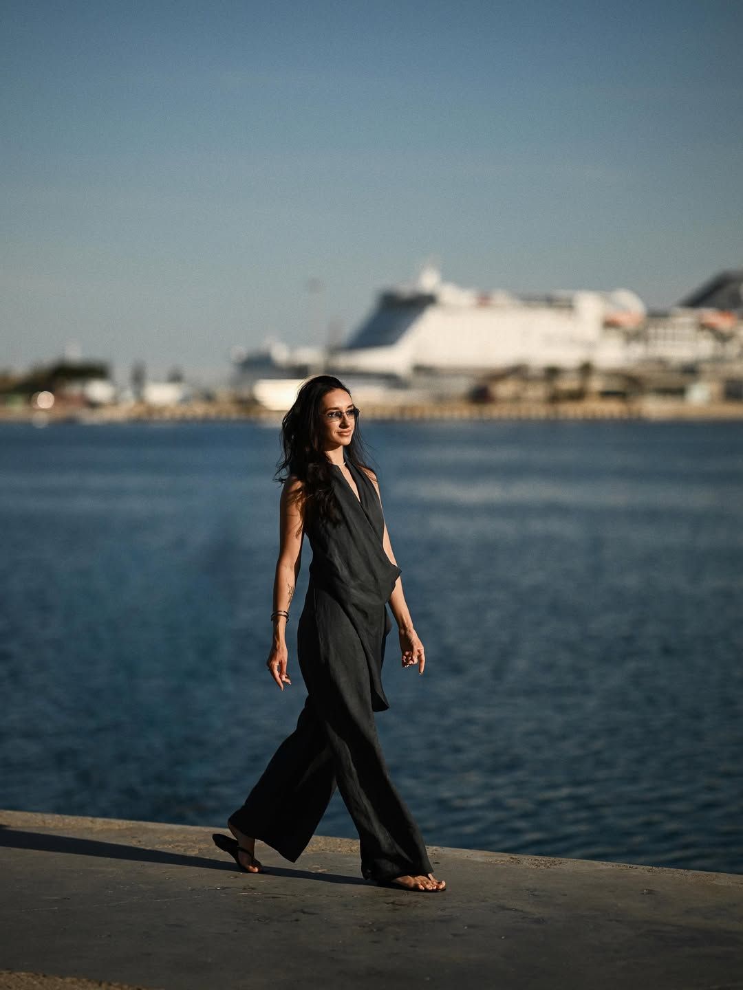 Elegant woman in a dark dress walking along the waterfront at Valencia Marina with a white ship in the background