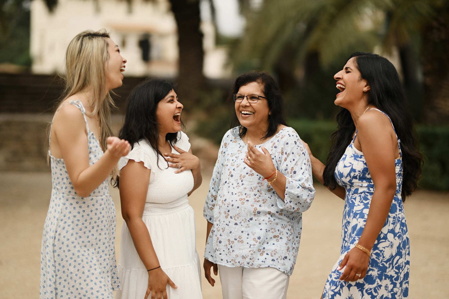 Four women from a diverse international family sharing a genuine, joyful laugh during a candid outdoor family photoshoot in Valencia.