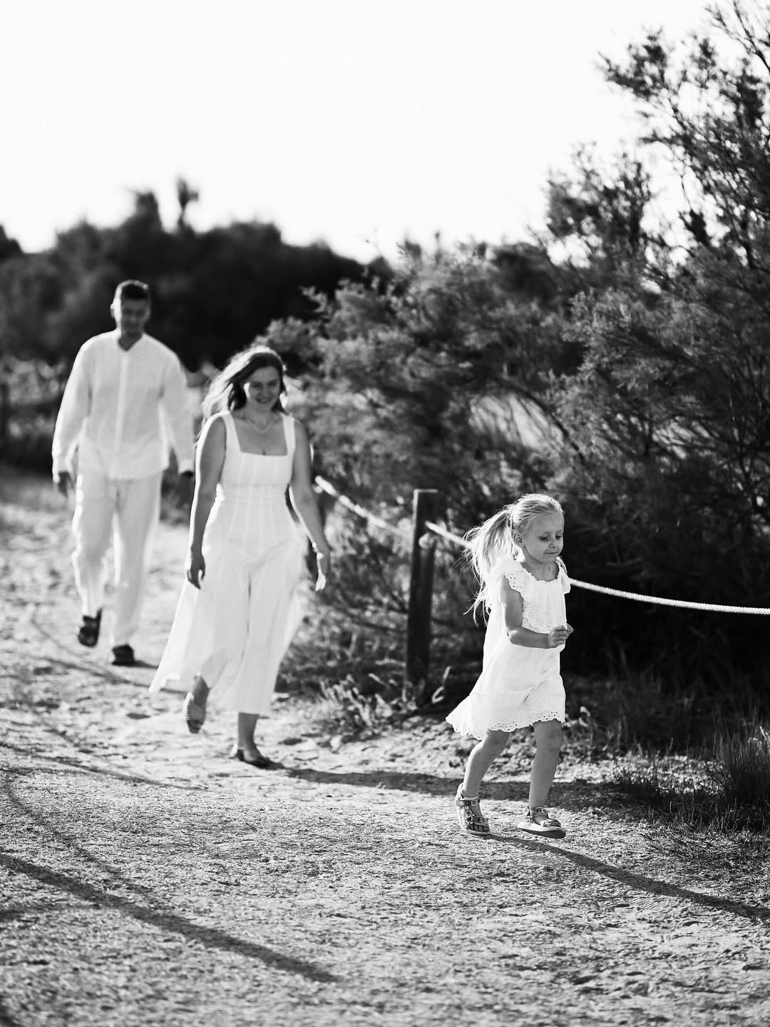A family of three running together along a dirt path lined with coastal vegetation in El Saler natural park.