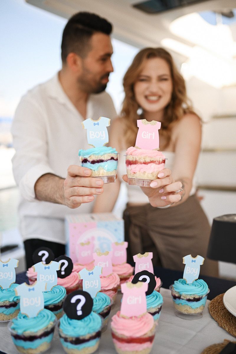Expecting couple holding boy and girl themed desserts on a private yacht in Valencia during their gender reveal party.
