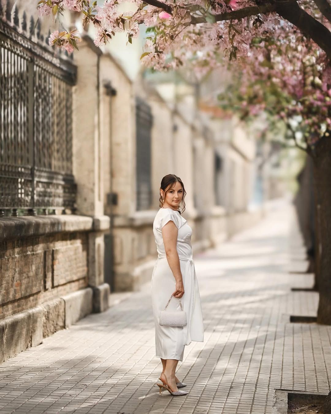 Woman walking down a beautiful Valencia street lined with pink spring blossoms and historic architecture for a solo portrait