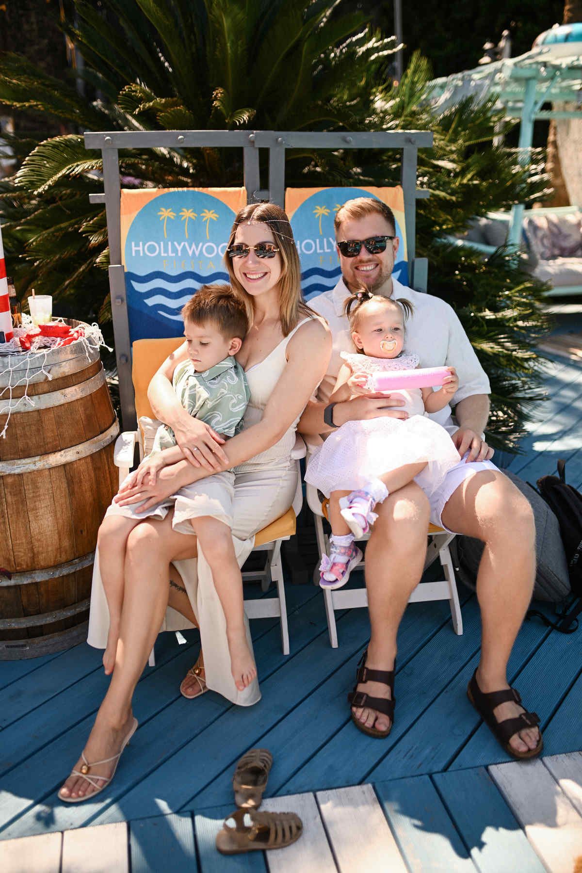 A relaxed family with two children sitting together in lounge chairs during an outdoor resort-style birthday party.