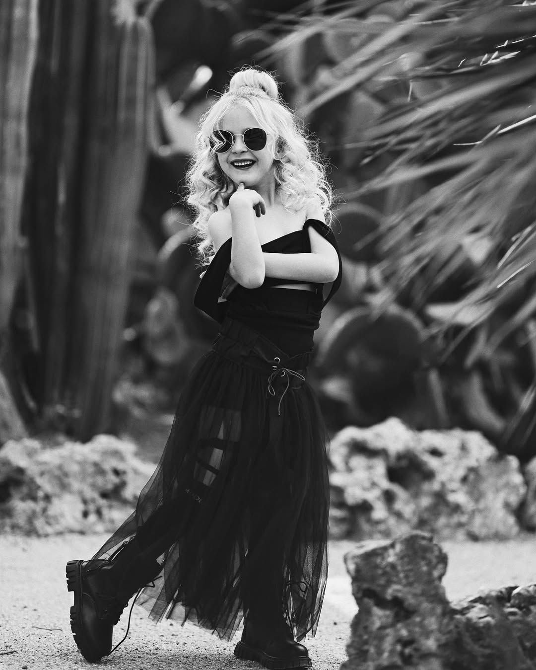 A young girl in a stylish black dress posing confidently among exotic plants at the Valencia Botanical Garden.