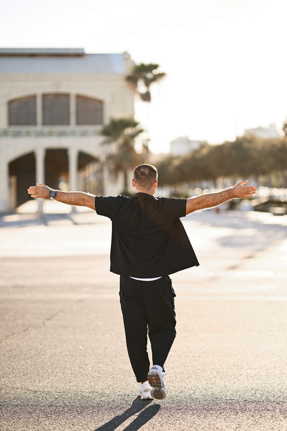 Back view of a casual man walking down a Valencia street with his arms wide open, capturing a carefree lifestyle vibe