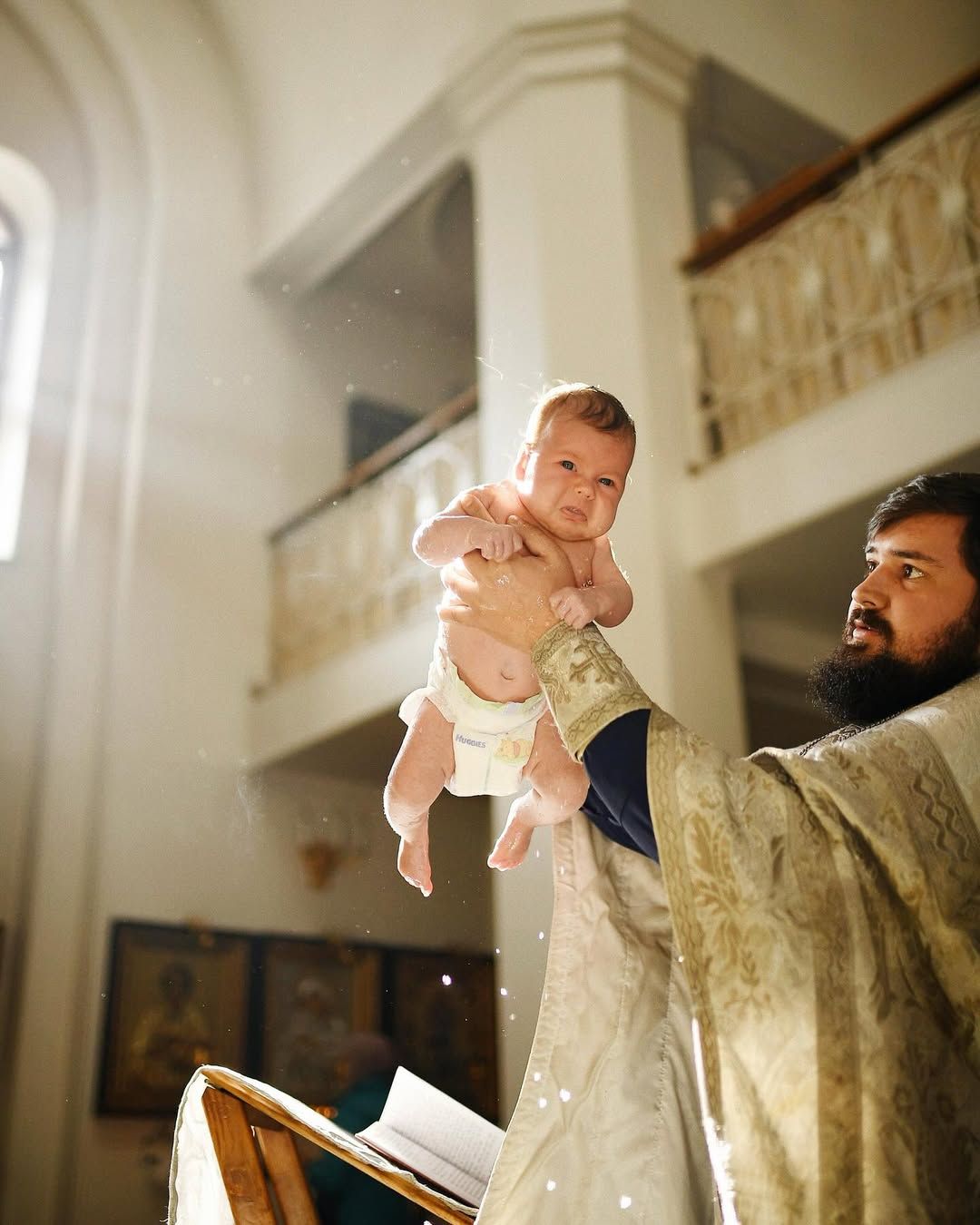 Priest holding a baby during the holy water baptism ritual inside a light-filled church in Valencia