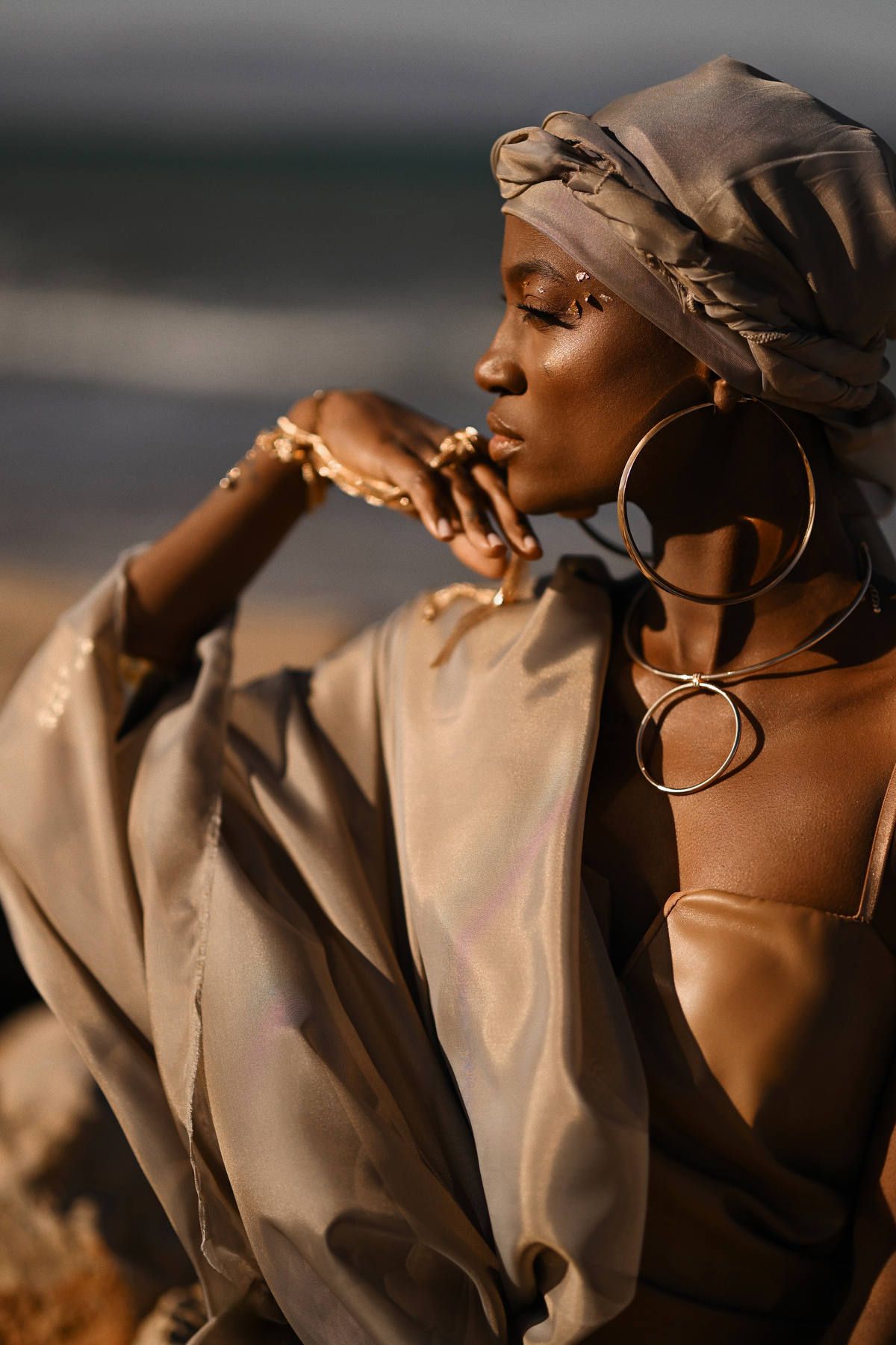 Close-up beauty portrait of a model with professional gold makeup and silk headwrap for high-end fashion campaigns.