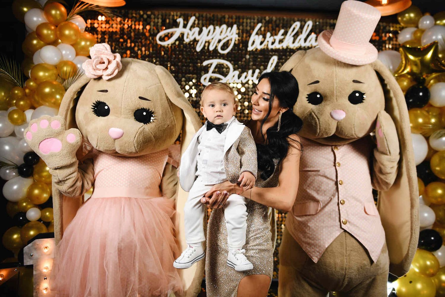 A mother and baby posing with two giant plush rabbit animators at a lavish children's birthday party.