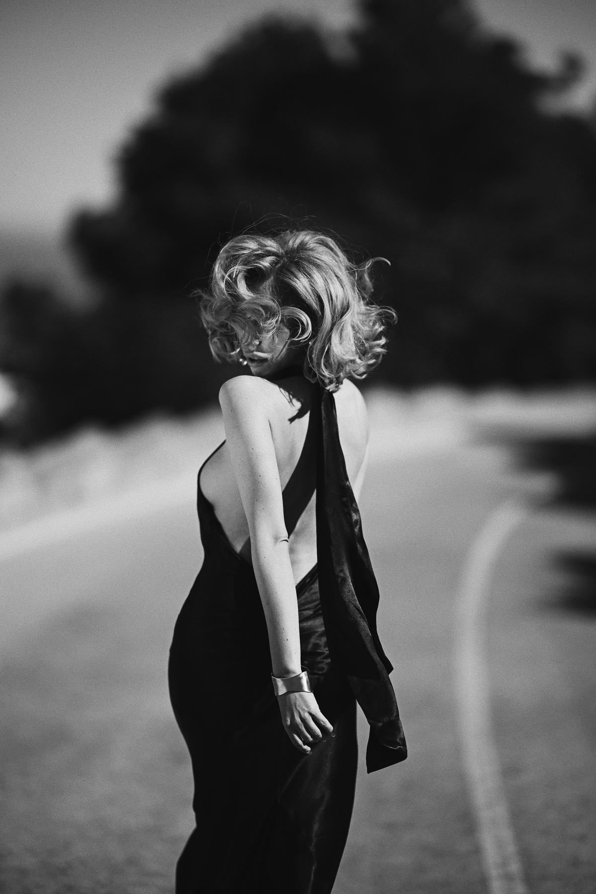 Cinematic black and white portrait of a woman looking over her shoulder with windblown hair on a coastal road in Javea
