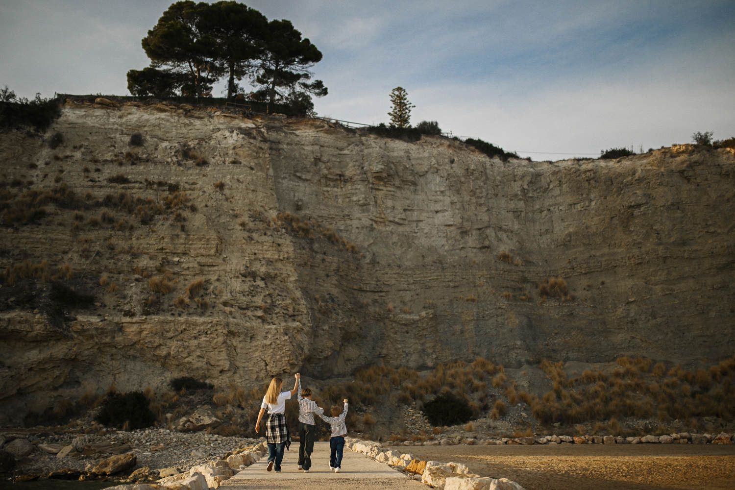Wide shot of a mother and her boys walking on a coastal path with the dramatic cliffs of Calpe towering in the background