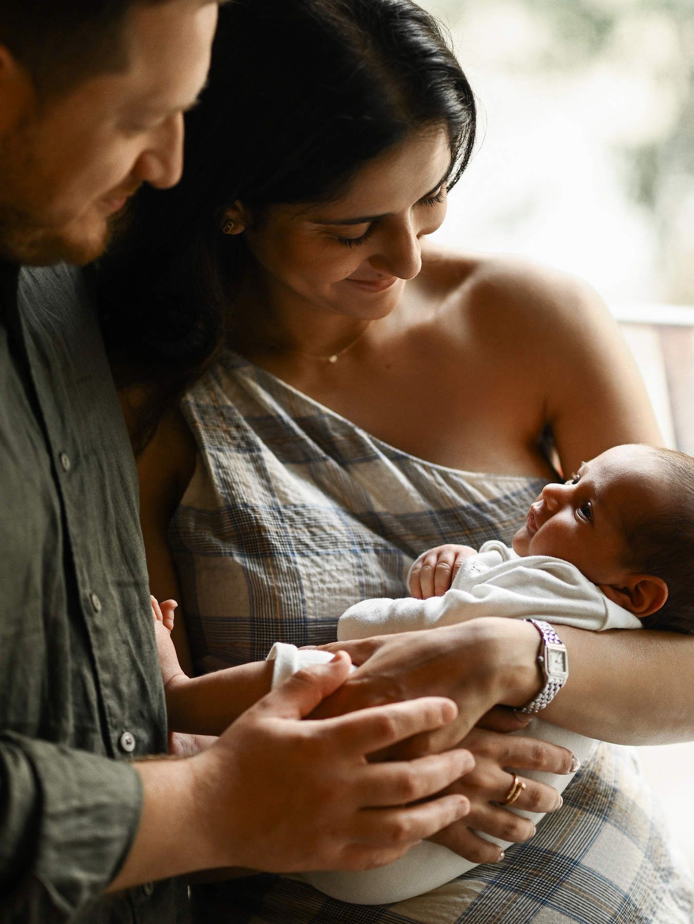 Newborn and baby photography in Valencia featuring a happy mother and father tenderly holding their wrapped infant together.