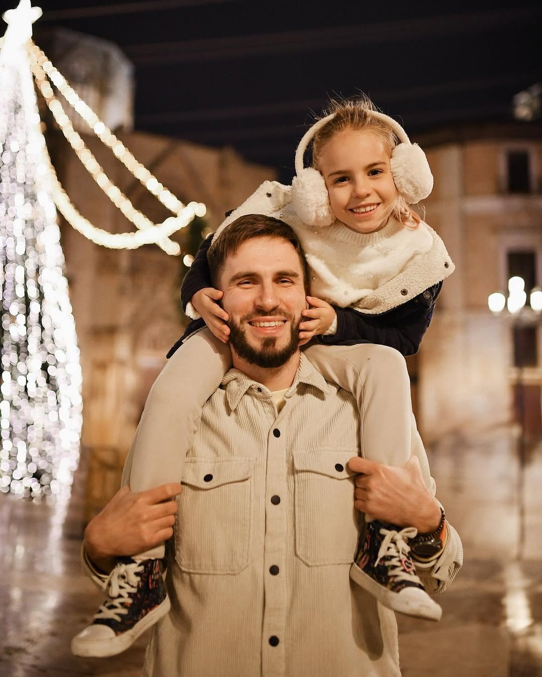Smiling father carrying his happy daughter on his shoulders during a festive Christmas evening photoshoot in Valencia