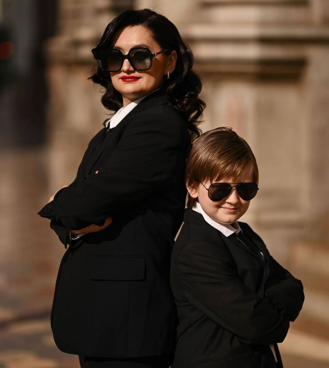A stylish mother and son in matching black suits and sunglasses, featured as a client testimonial for Darina Derzkaya's photography in Valen