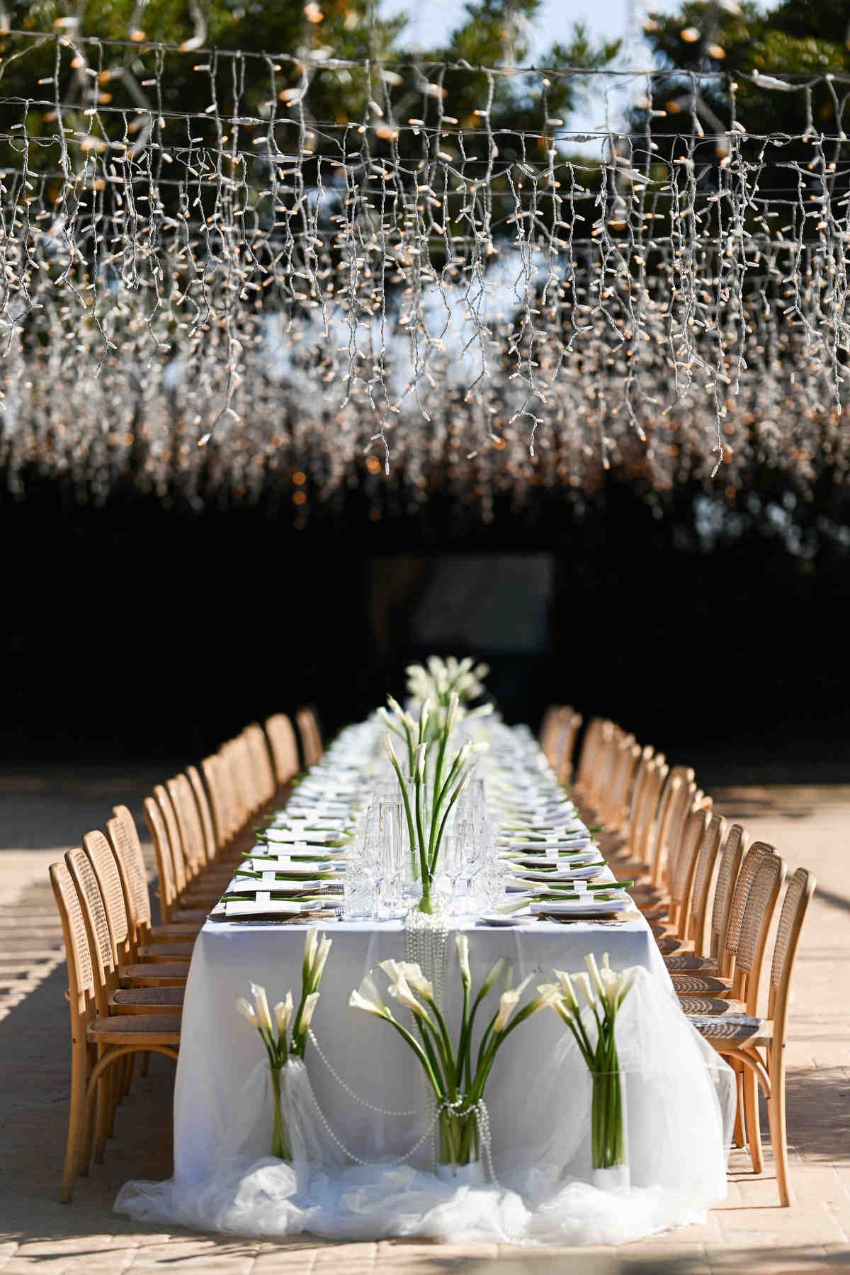 Endless wedding banquet table styled with white calla lilies under a spectacular canopy of hanging fairy lights.