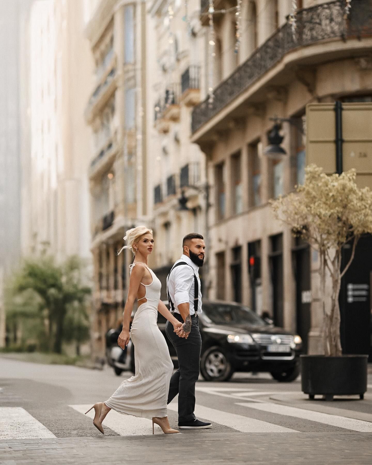 A stylish bride and groom holding hands while walking across a pedestrian crosswalk on a historic street in the center of Valencia.