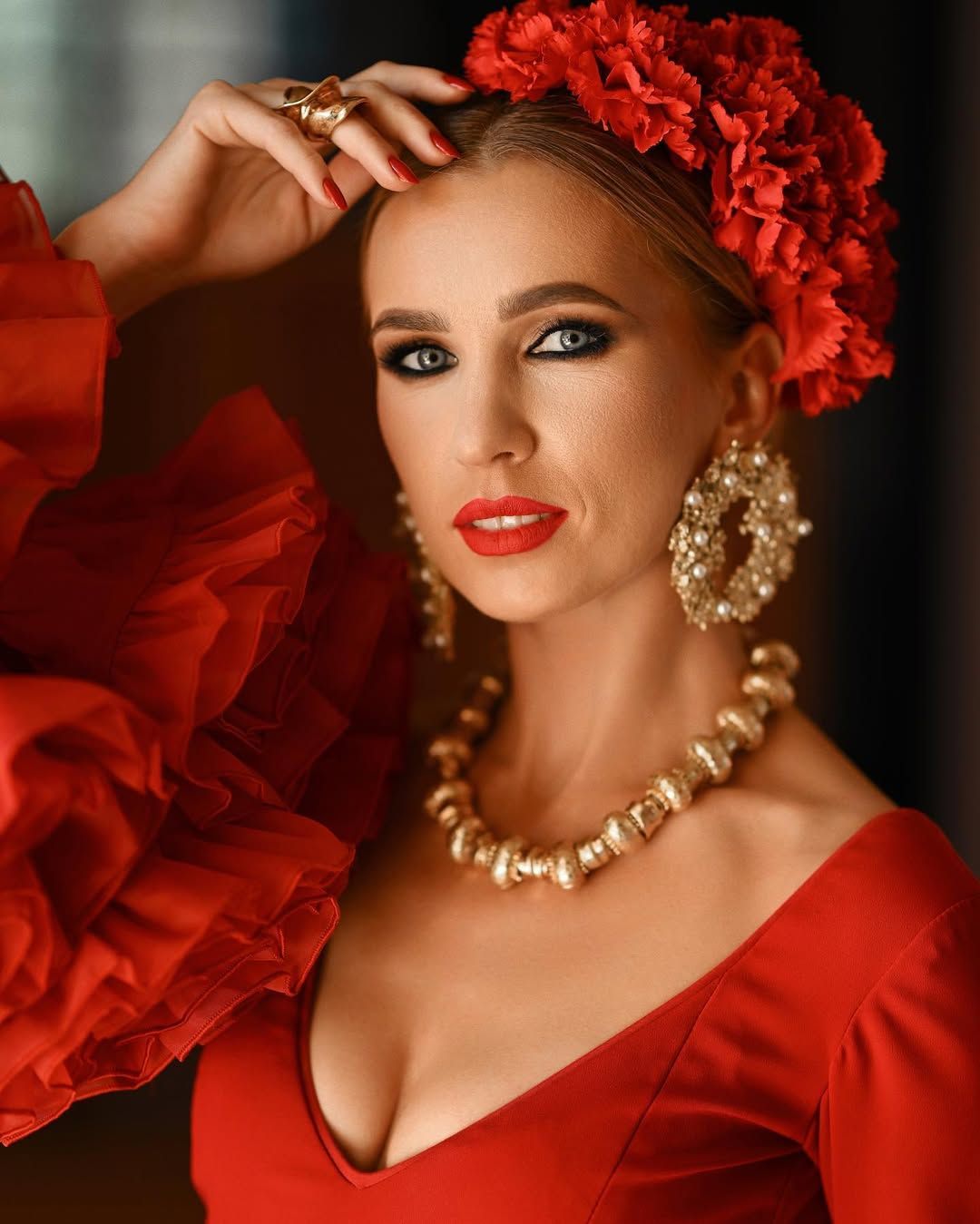 Close-up portrait of a woman wearing gold statement jewelry and a red flower hair accessory at Villa Montemolar.