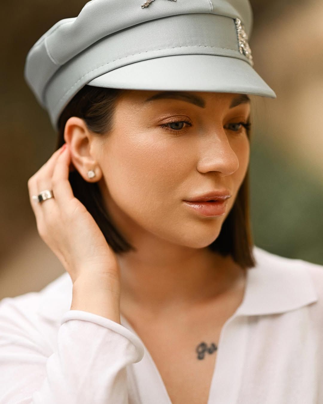 A close-up portrait of a woman wearing a stylish grey cap in the historic Monforte Gardens.