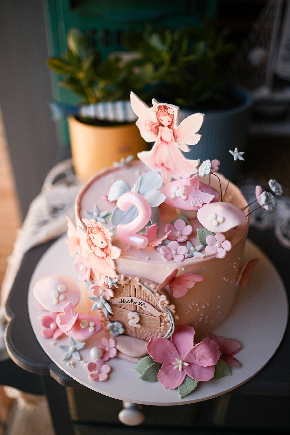Close-up of a premium pink birthday cake decorated with flowers, butterflies, and a fairy topper for a second birthday.