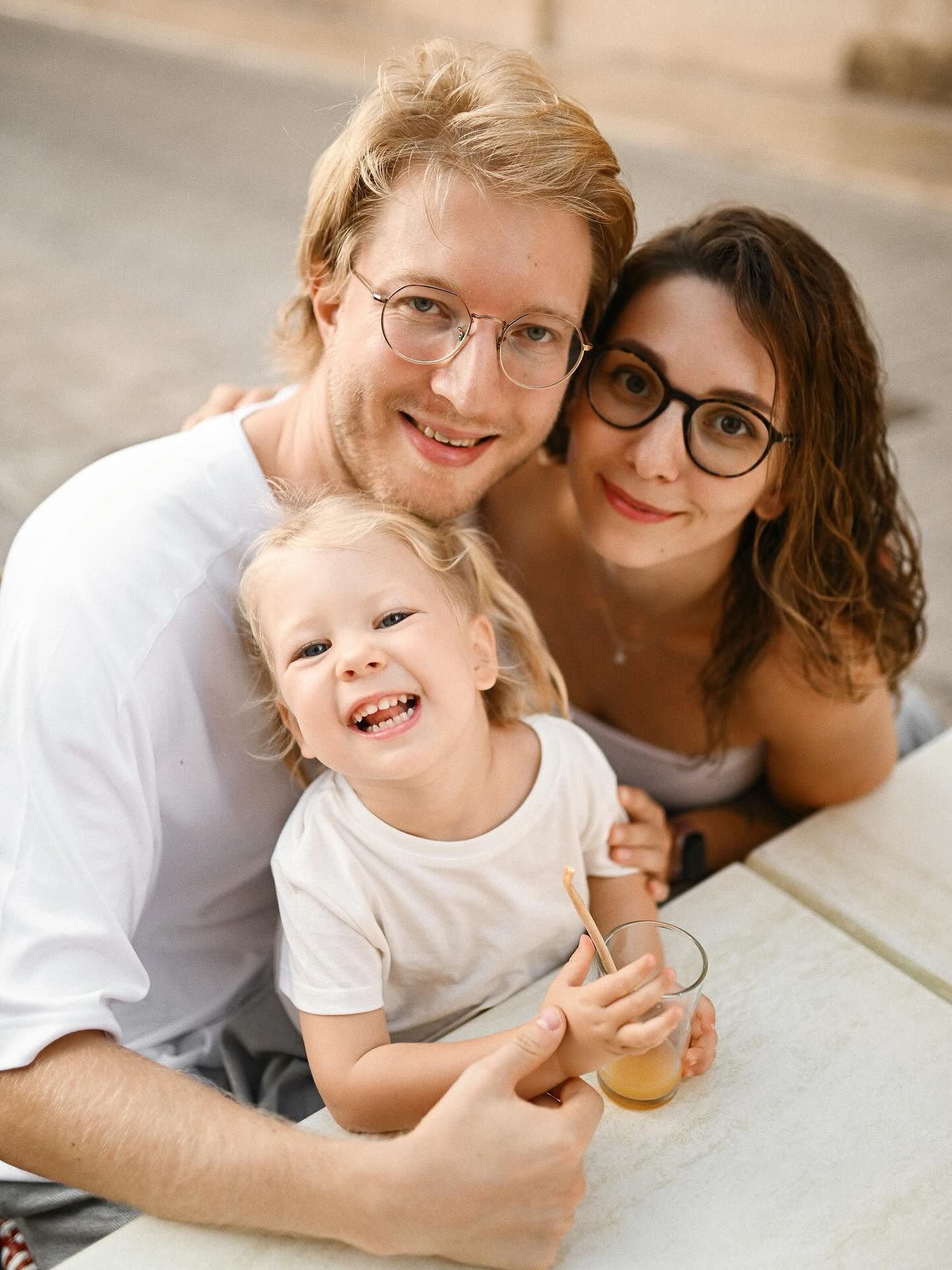 A happy couple sitting at an outdoor cafe with their laughing toddler, enjoying a relaxing break together during a city photoshoot.