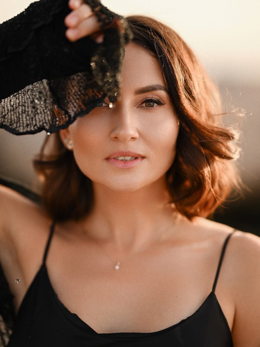 Close-up female portrait at a Valencia beach, woman holding a piece of black lace near her face creating sunset shadows.