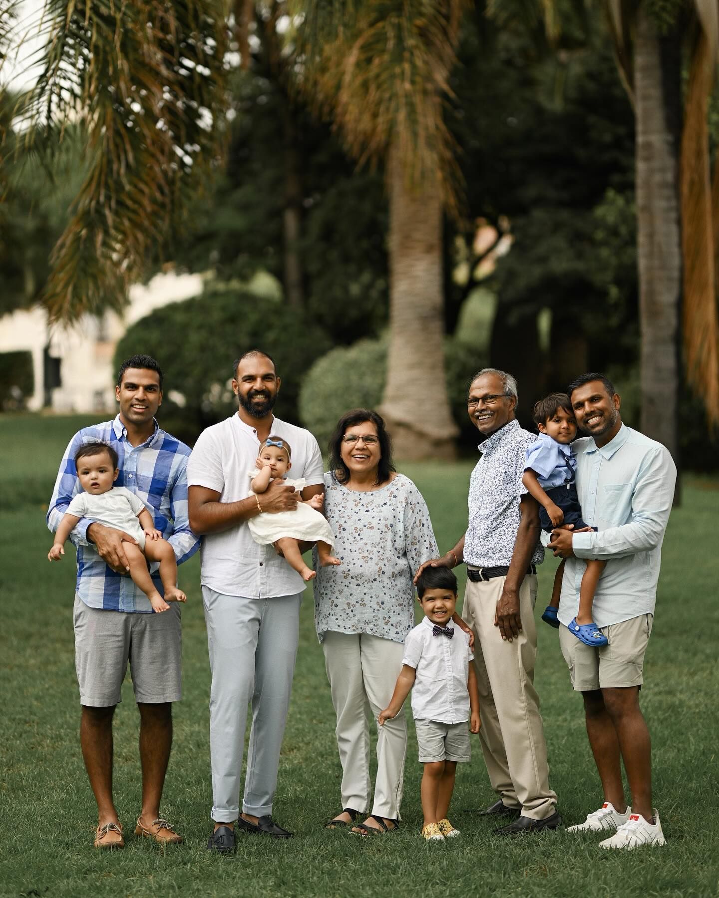 A large family with children posing together on the green grass in a park, celebrating their strong bond during an outdoor photoshoot.