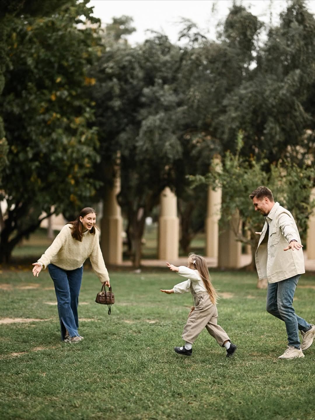 Family enjoying playful moments during a maternity photoshoot in Turia Park, Valencia, with open lawns and calm afternoon light.