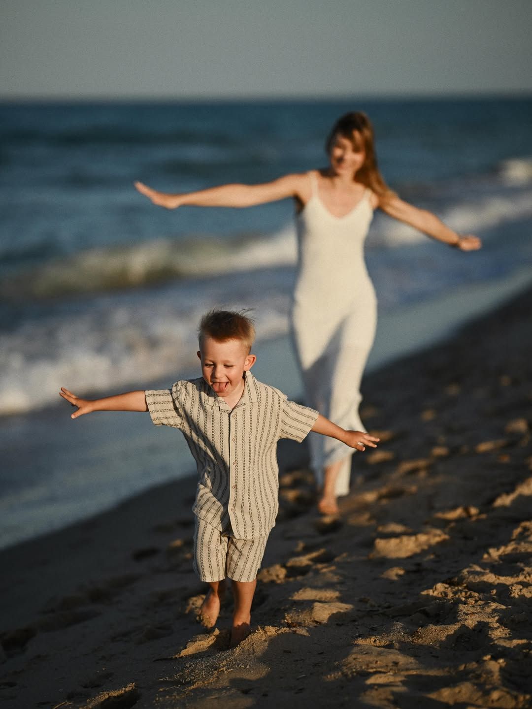 A playful boy runs across the sand with airplane arms while his mother follows during a fun family afternoon at El Saler.