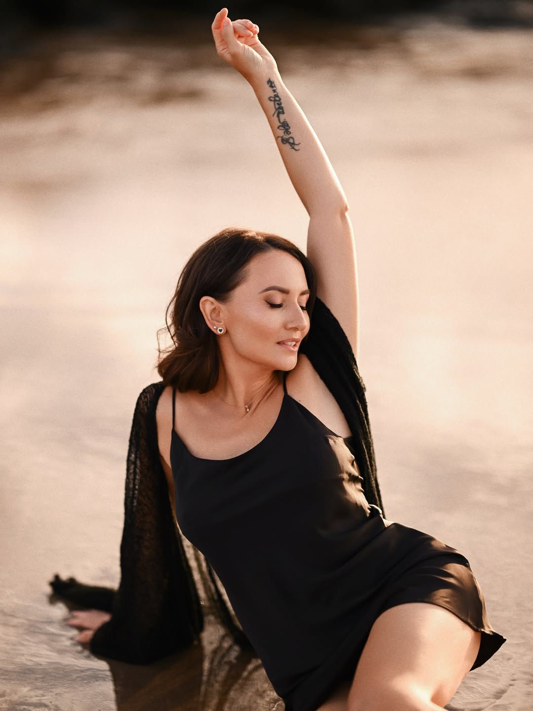 Artistic female portrait at a Valencia beach, woman sitting in shallow water with her arm raised and eyes gently closed.