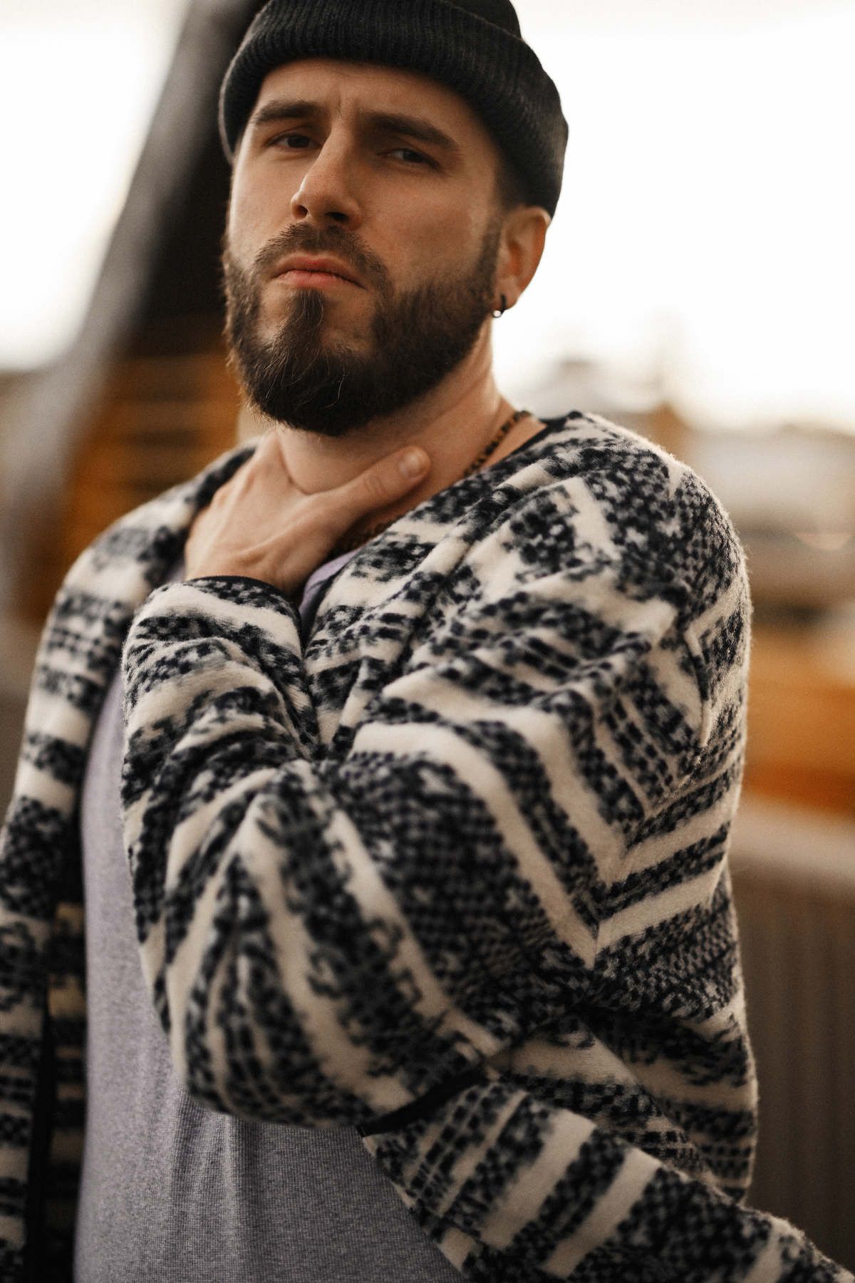 Authentic portrait of a man in a beanie and stylish sweater posing with his hand on his neck, looking into the camera lens.