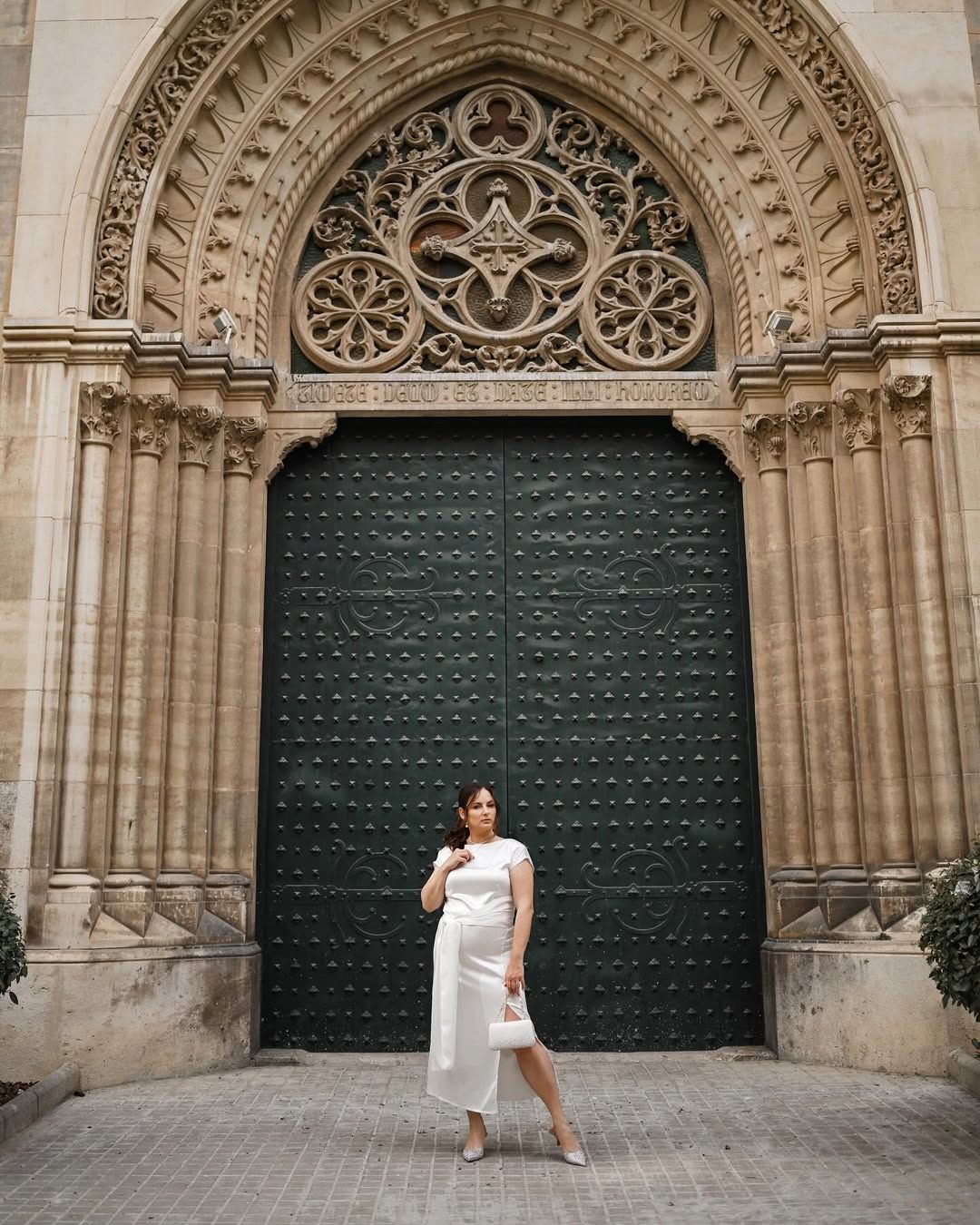 Elegant woman in a white silk dress standing in front of grand historic doors and gothic architecture in Valencia