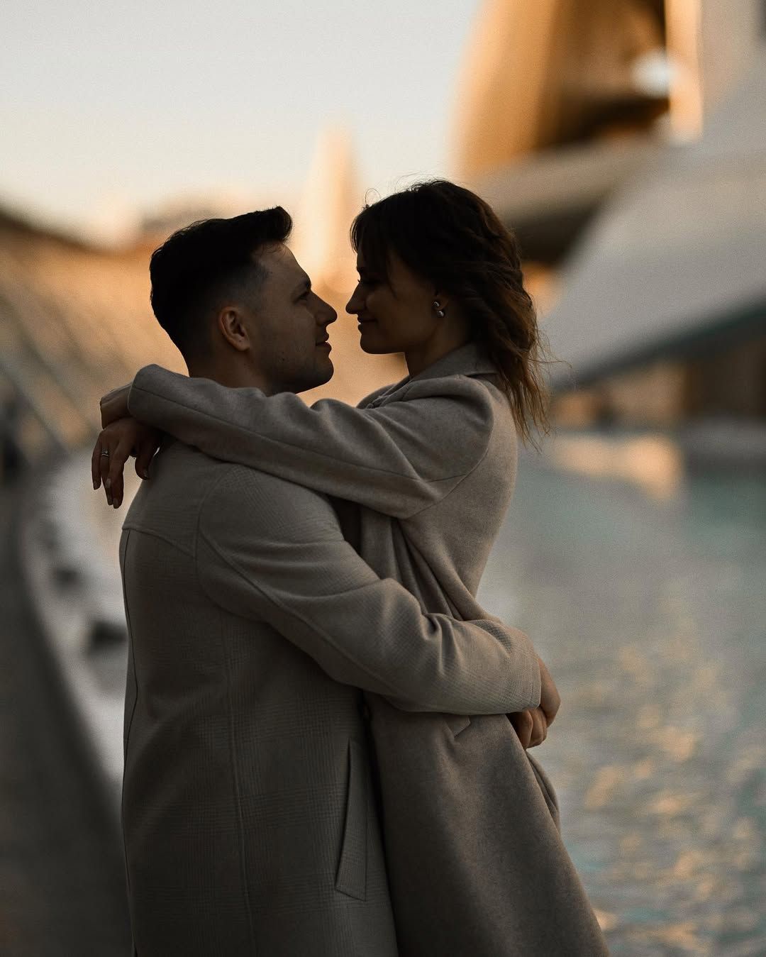 Engaged couple hugging closely beside a turquoise reflective pool at dusk during their destination session in Valencia.
