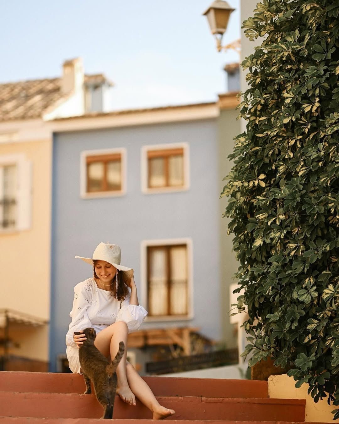 Candid shot of a woman petting a cat on the charming stone stairs of a narrow pedestrian street in Port Saplaya, Valencia