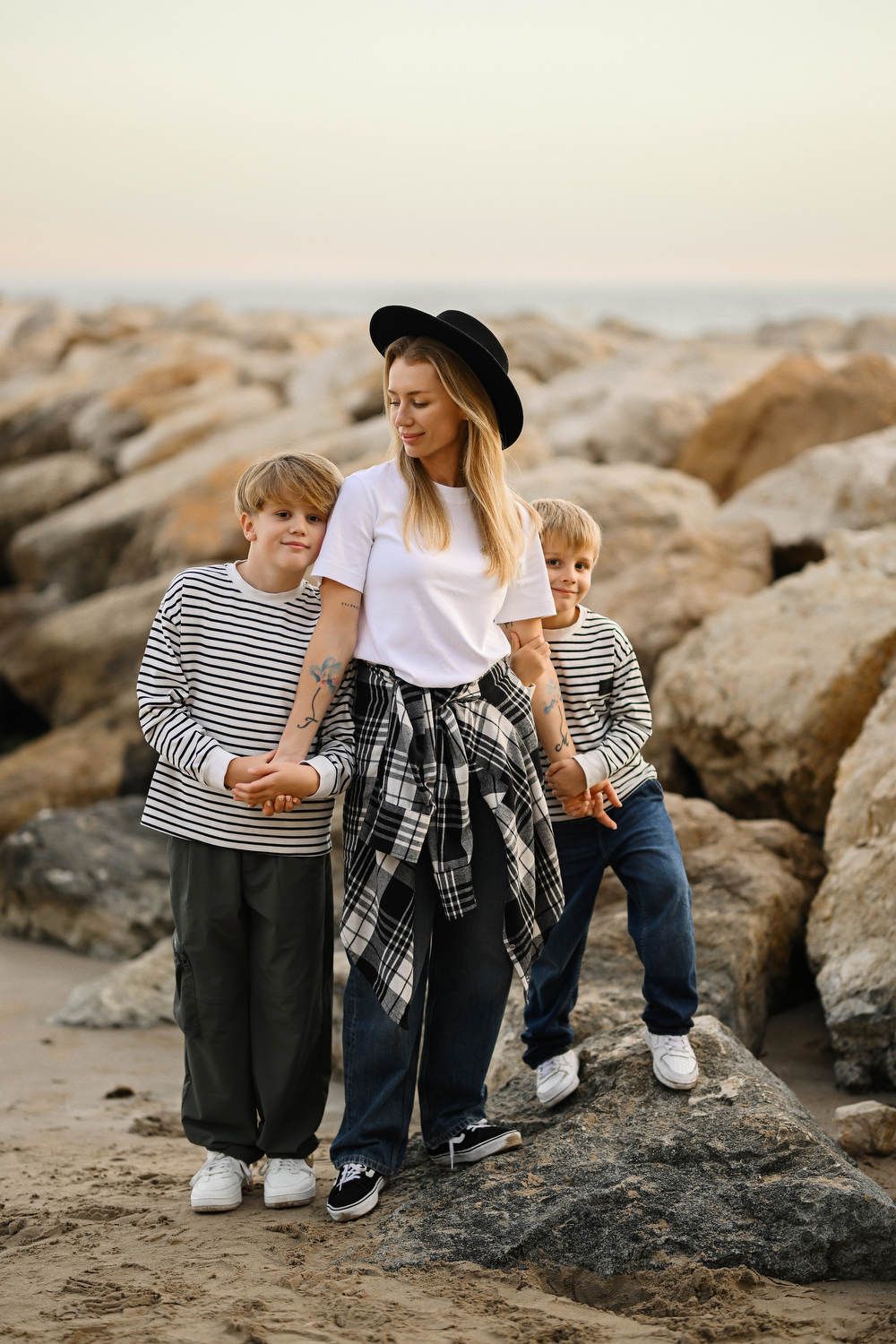A stylish mother and her two sons posing playfully on the large rocks at the beach during a relaxed Calpe family photoshoot