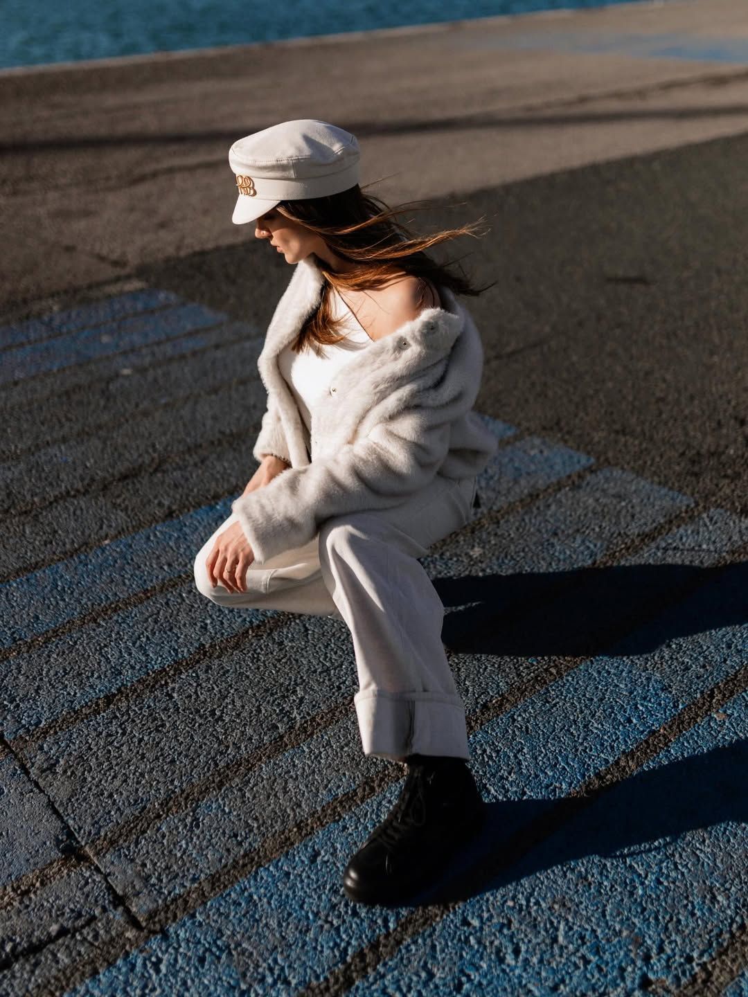 Fashion portrait of a woman in a white outfit posing on blue textured ground at Valencia Marina