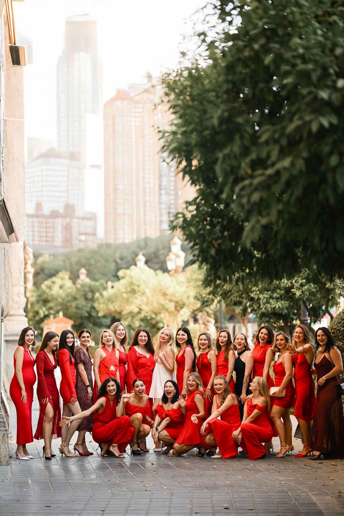 A large group of cheerful women in elegant red dresses posing outdoors for a milestone adult birthday celebration photo.