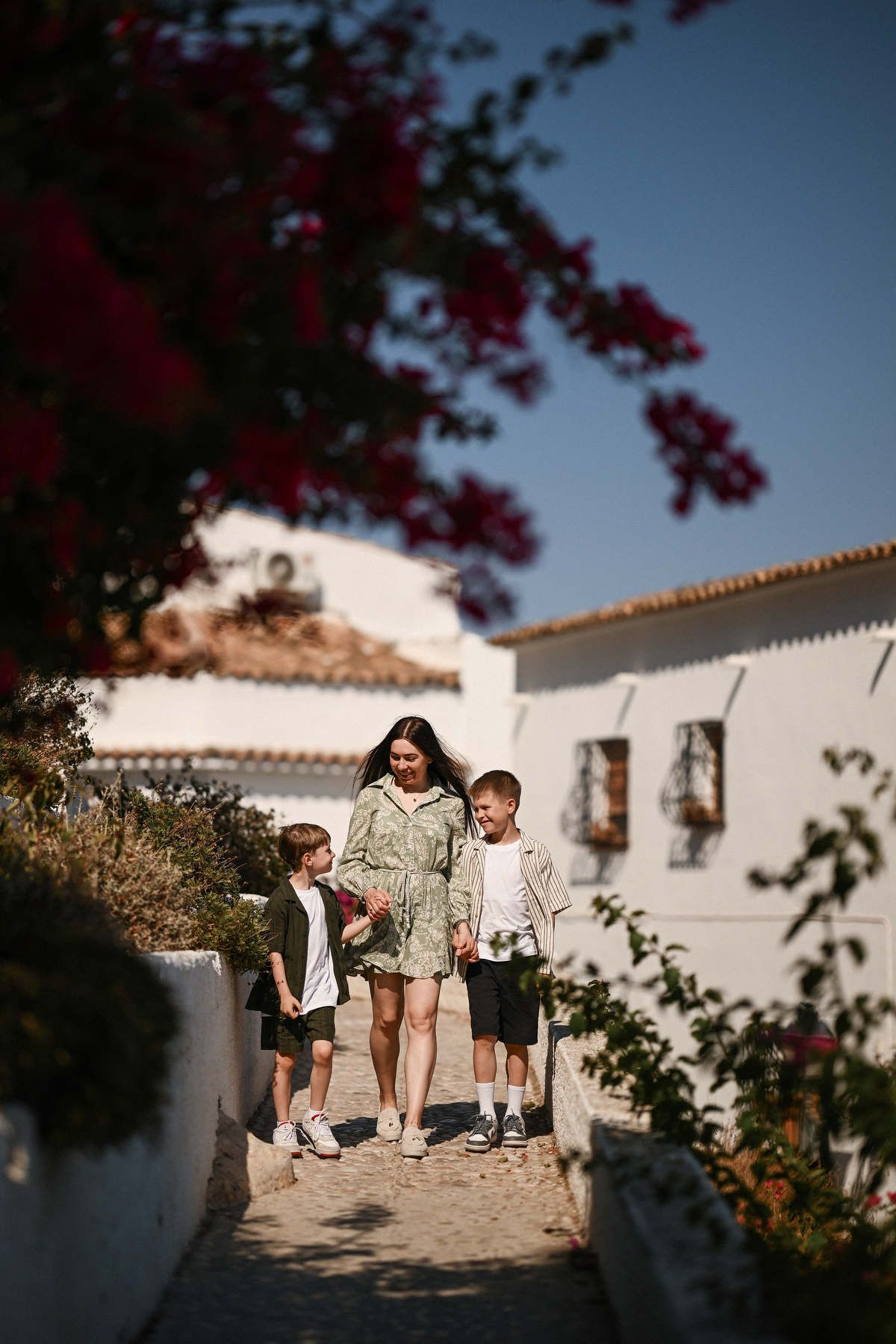 Mother walking hand-in-hand with her sons through a pedestrian-friendly white alleyway in Altea's historic center.