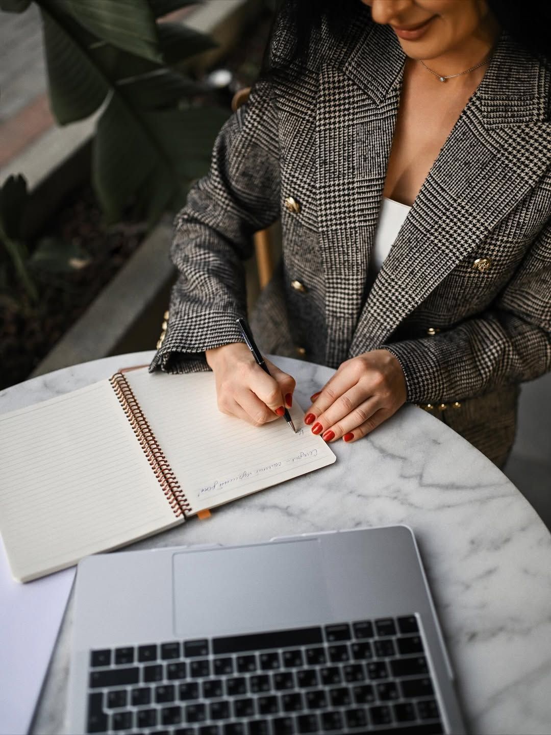 A mentor writing in a notebook next to a laptop, perfect for newsletters and creative content planning.